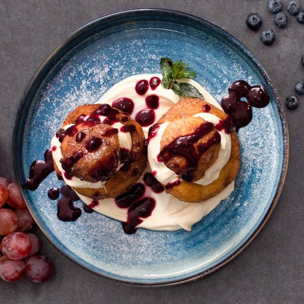 Papanași cu brânză serviți cu smântână și sos de fructe de pădure